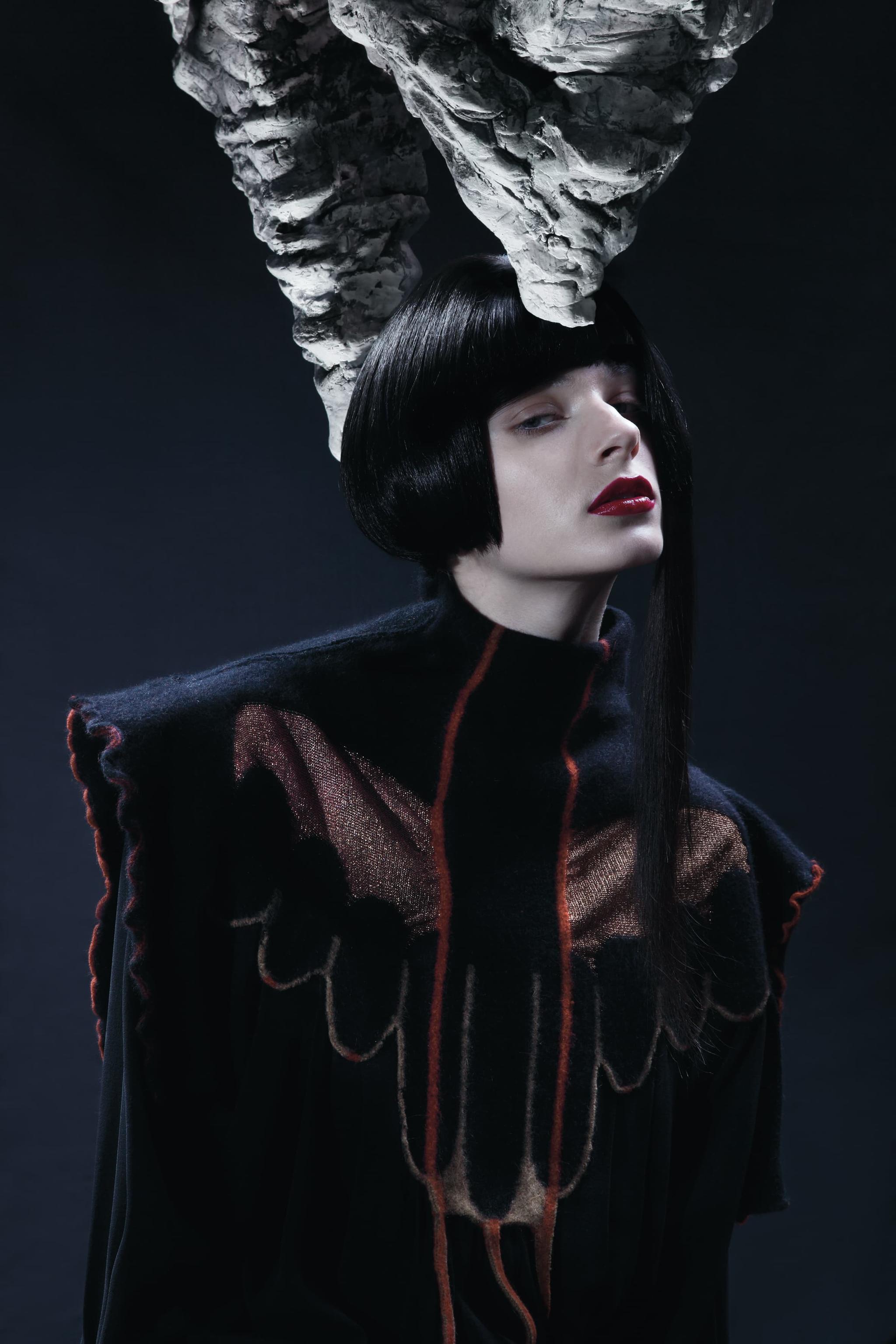 young woman, straight black haircut, dark red lips, pale skin, dark red design with wool, copper, silk